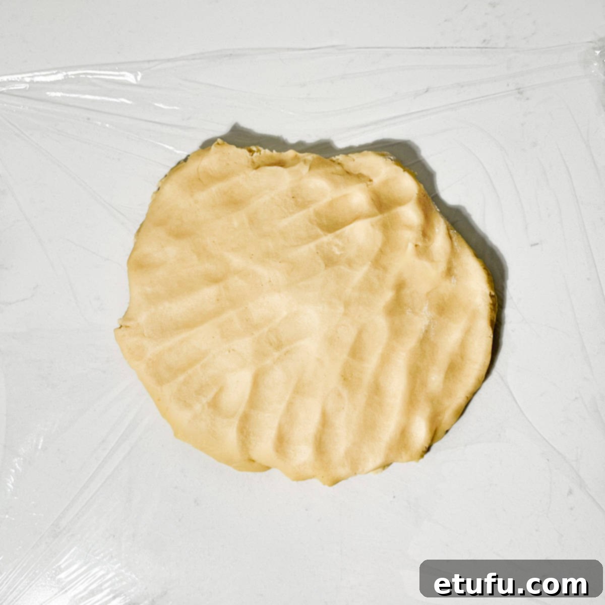 The flattened pastry dough wrapped in cling film, chilling in the refrigerator.