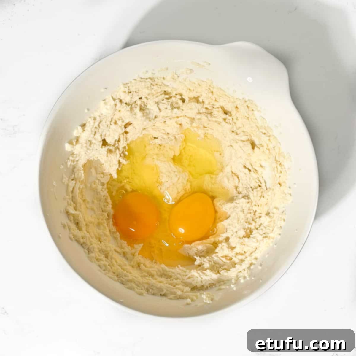 Adding room temperature eggs to the frangipane mixture in a white bowl.