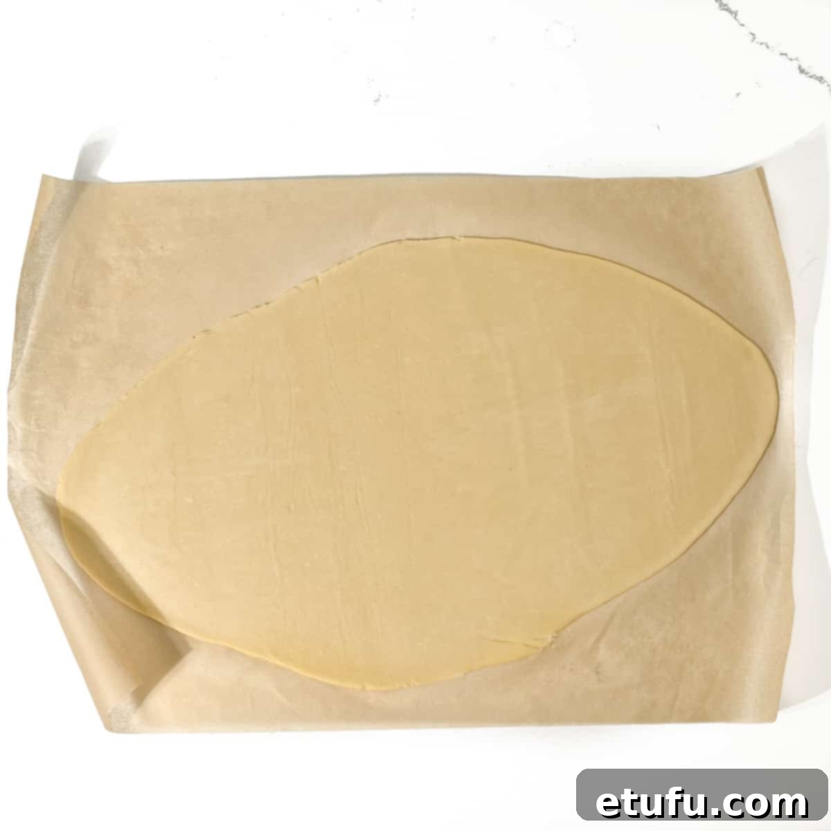 Rolled out pastry dough on baking paper, perfectly thin and ready for cutting.