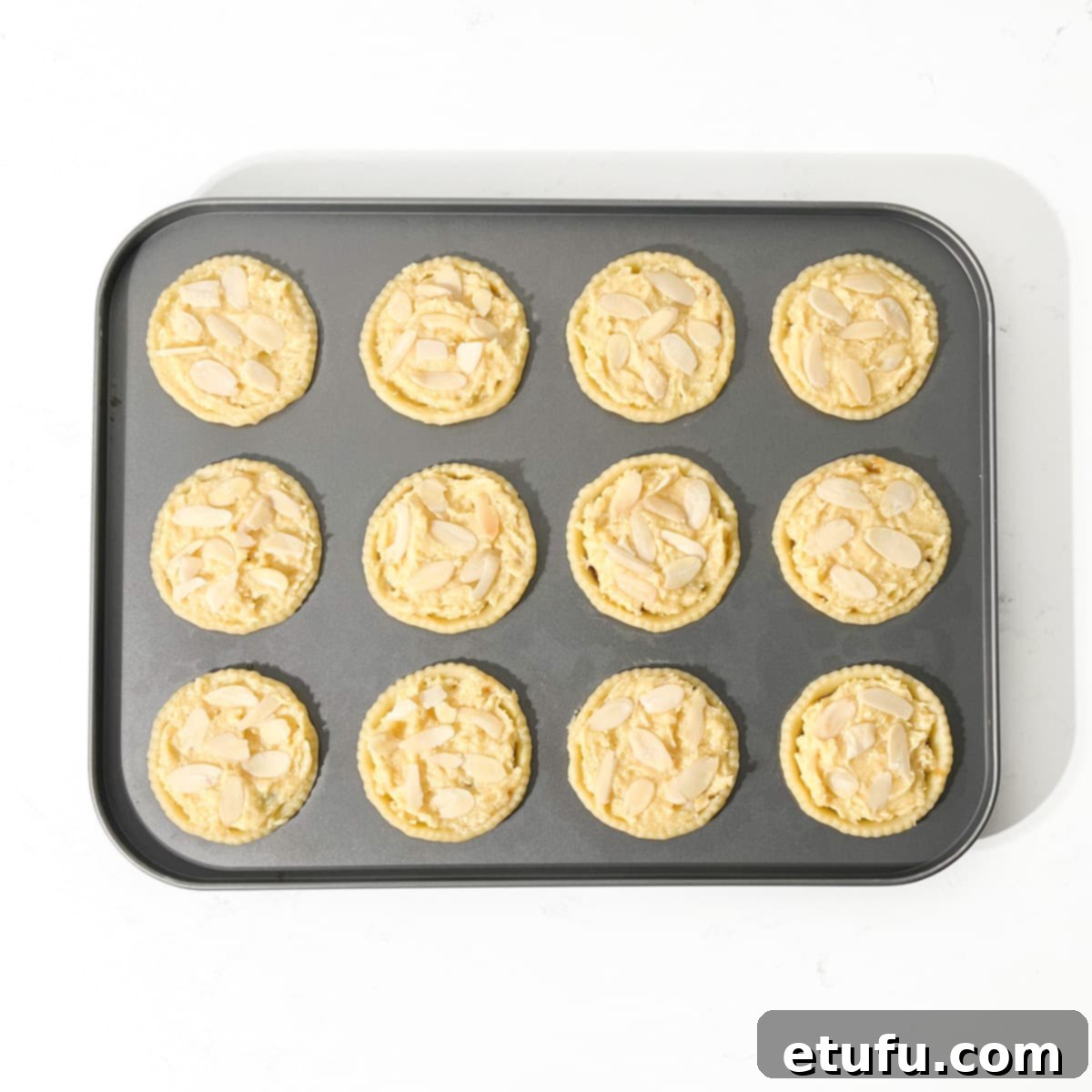 Unbaked mince pies topped with frangipane and scattered with flaked almonds.