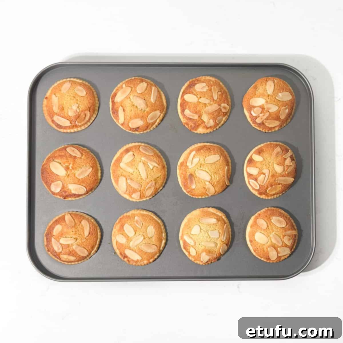 Freshly baked frangipane mince pies, golden and puffed, cooling in the tin.