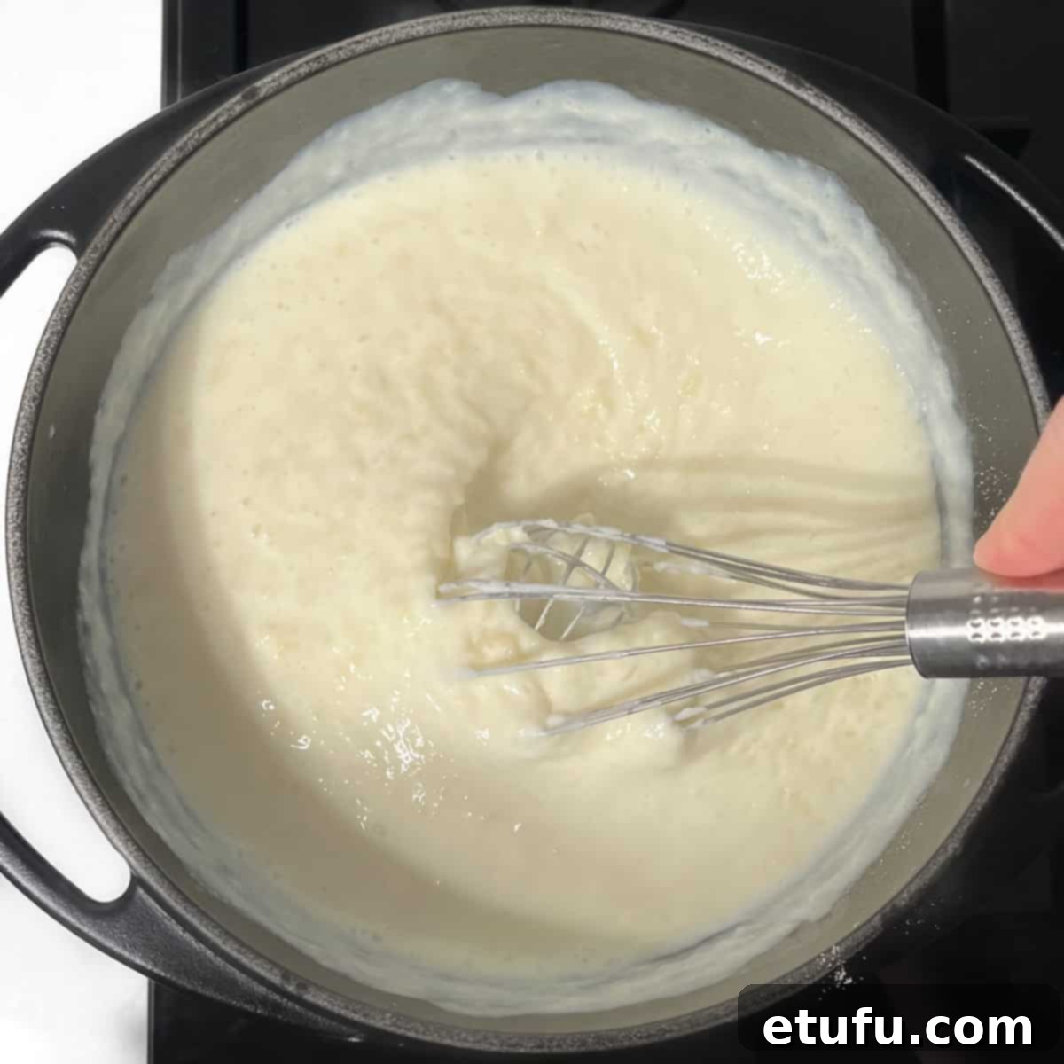 A whisk vigorously mixing Melkkos in a black saucepan, ensuring a smooth, lump-free consistency.