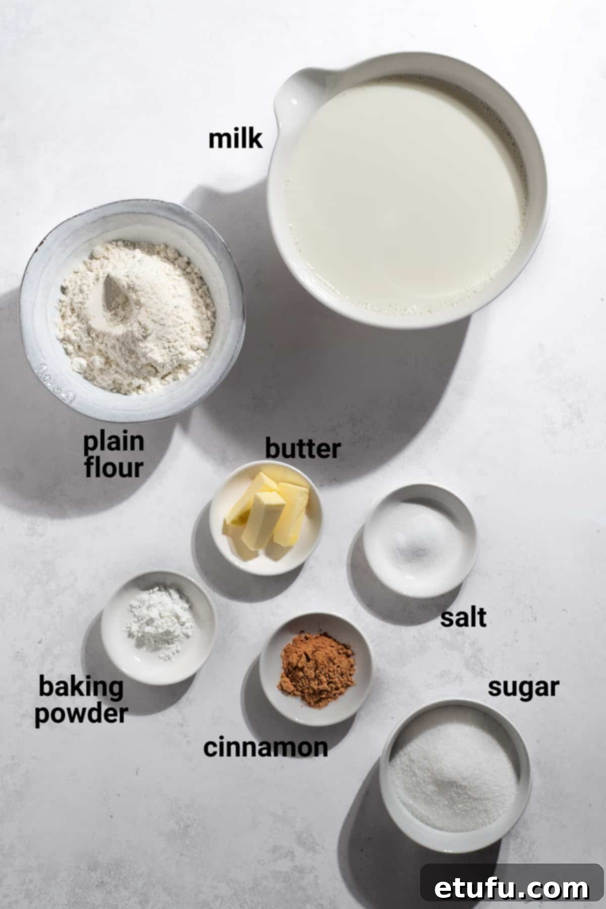 Essential ingredients for Melkkos, including milk, flour, butter, sugar, and cinnamon, arranged on a rustic wooden surface.