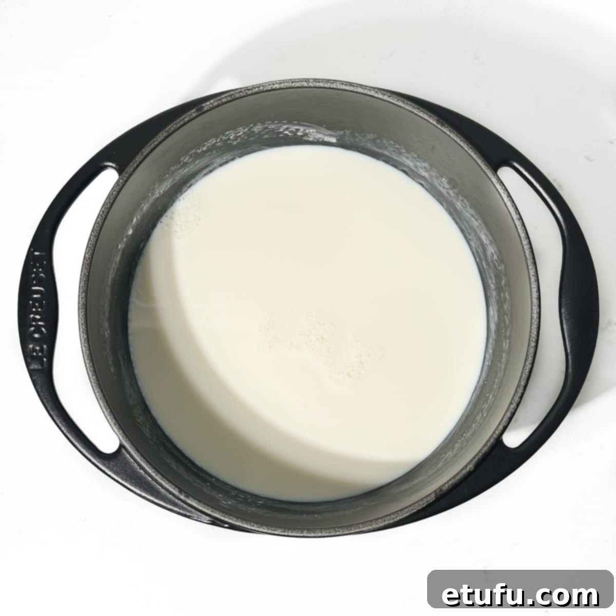 Fresh milk gently simmering in a black saucepan, creating a light froth on the surface, ready for Melkkos preparation.