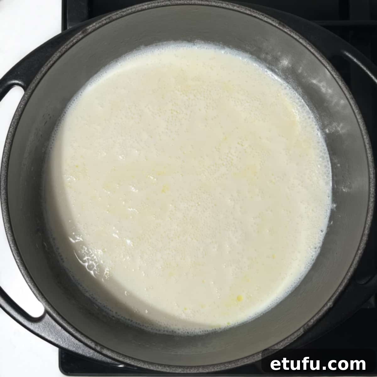 Milk gently boiling and frothy in a black saucepan, indicating it's reached the perfect temperature for the next step of making Melkkos.