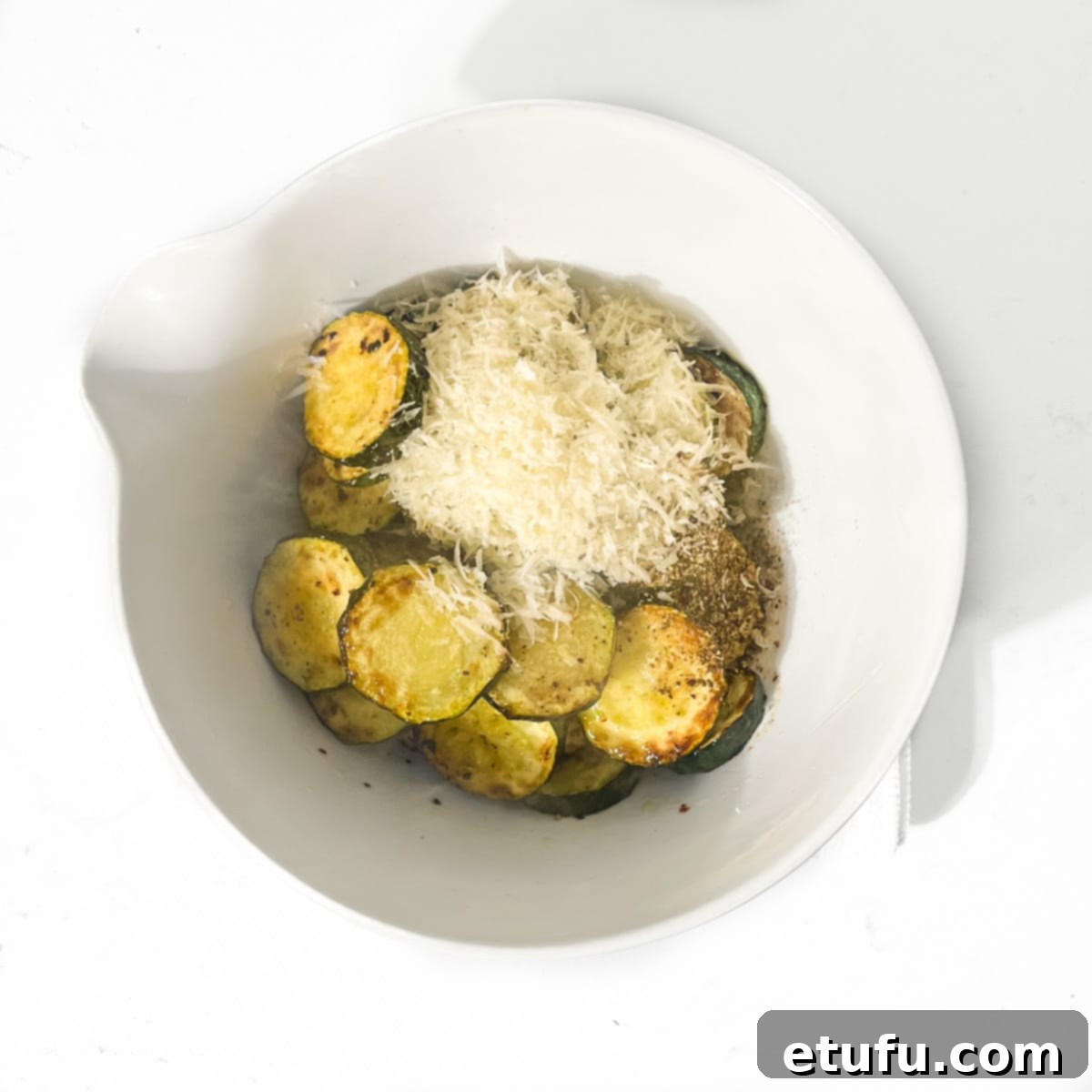 Crispy Fried Zucchini 11 Adding grated Parmesan cheese to fried courgettes in a small white bowl.