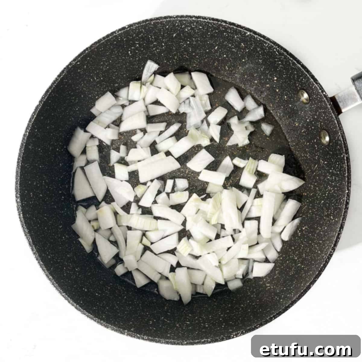 Onions added to hot oil in a frying pan.