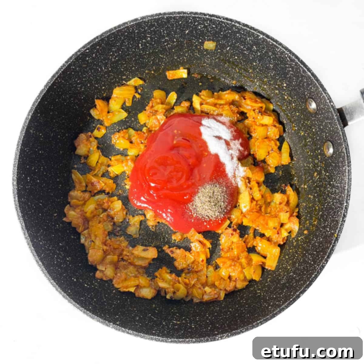 Tomato ketchup added to the spicy onions in a frying pan.
