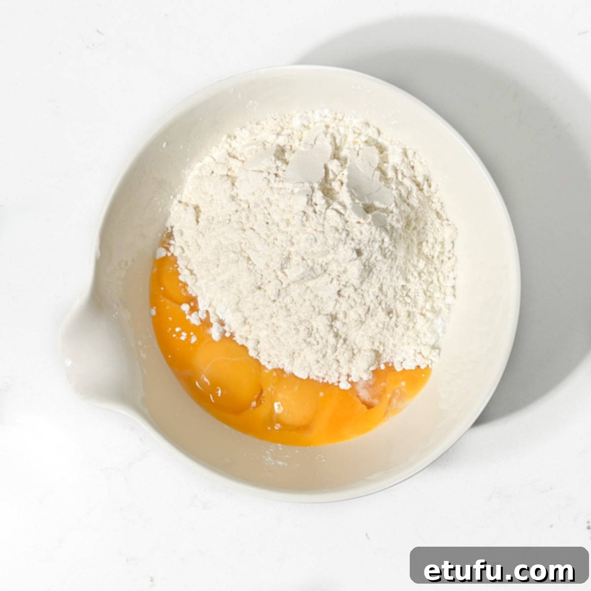 Egg yolks, sugar and slours in a small white mixing bowl.