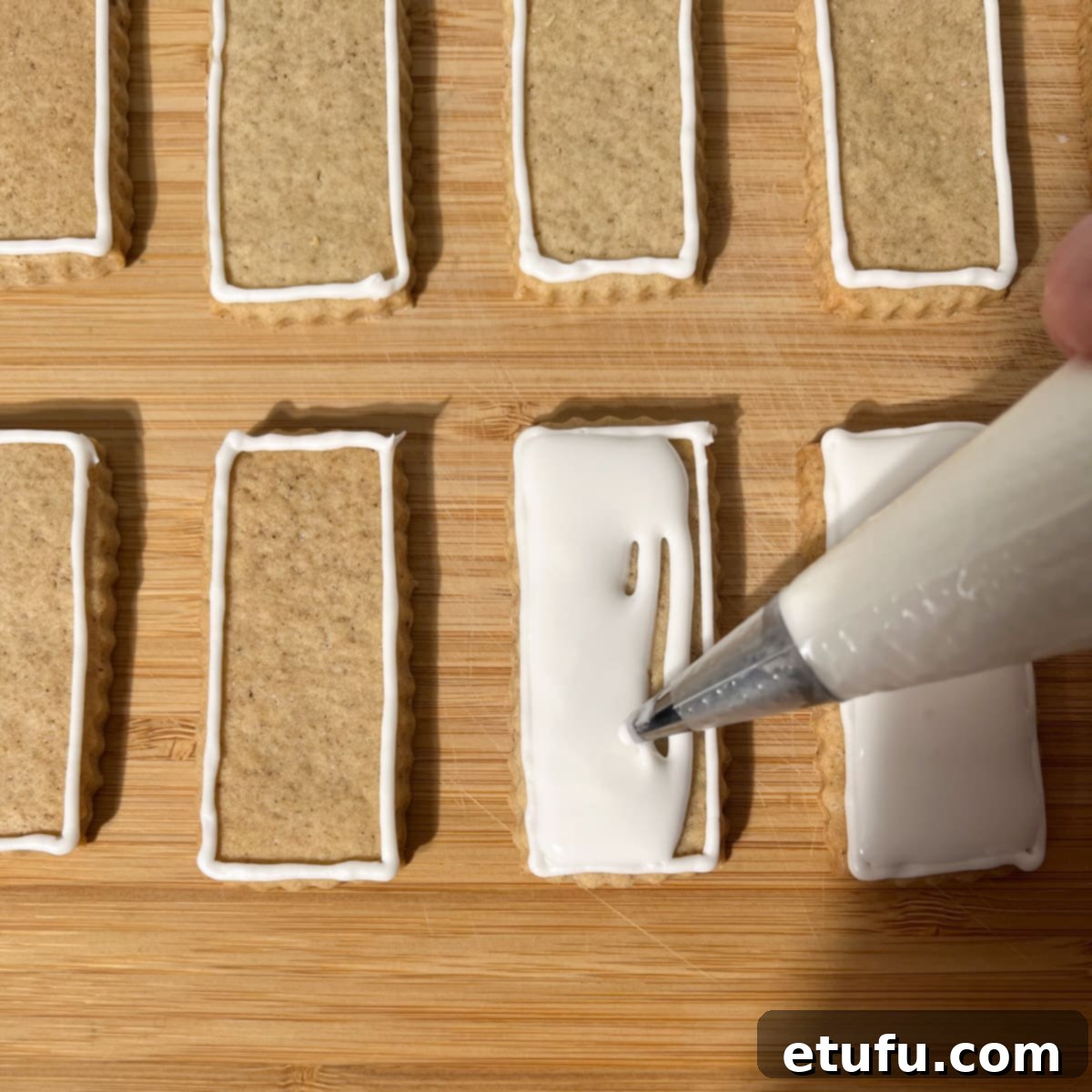 Spreading the royal icing across the cookie surface with the tip of the piping tip to fill gaps smoothly.