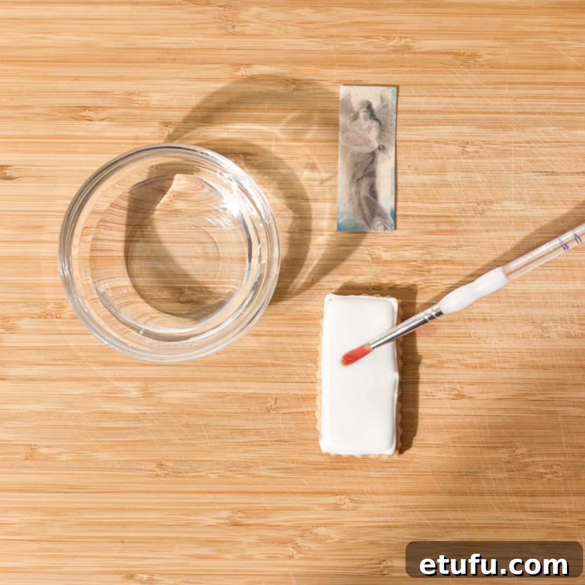Applying water with a small clean brush on top of the hardened cookie icing.