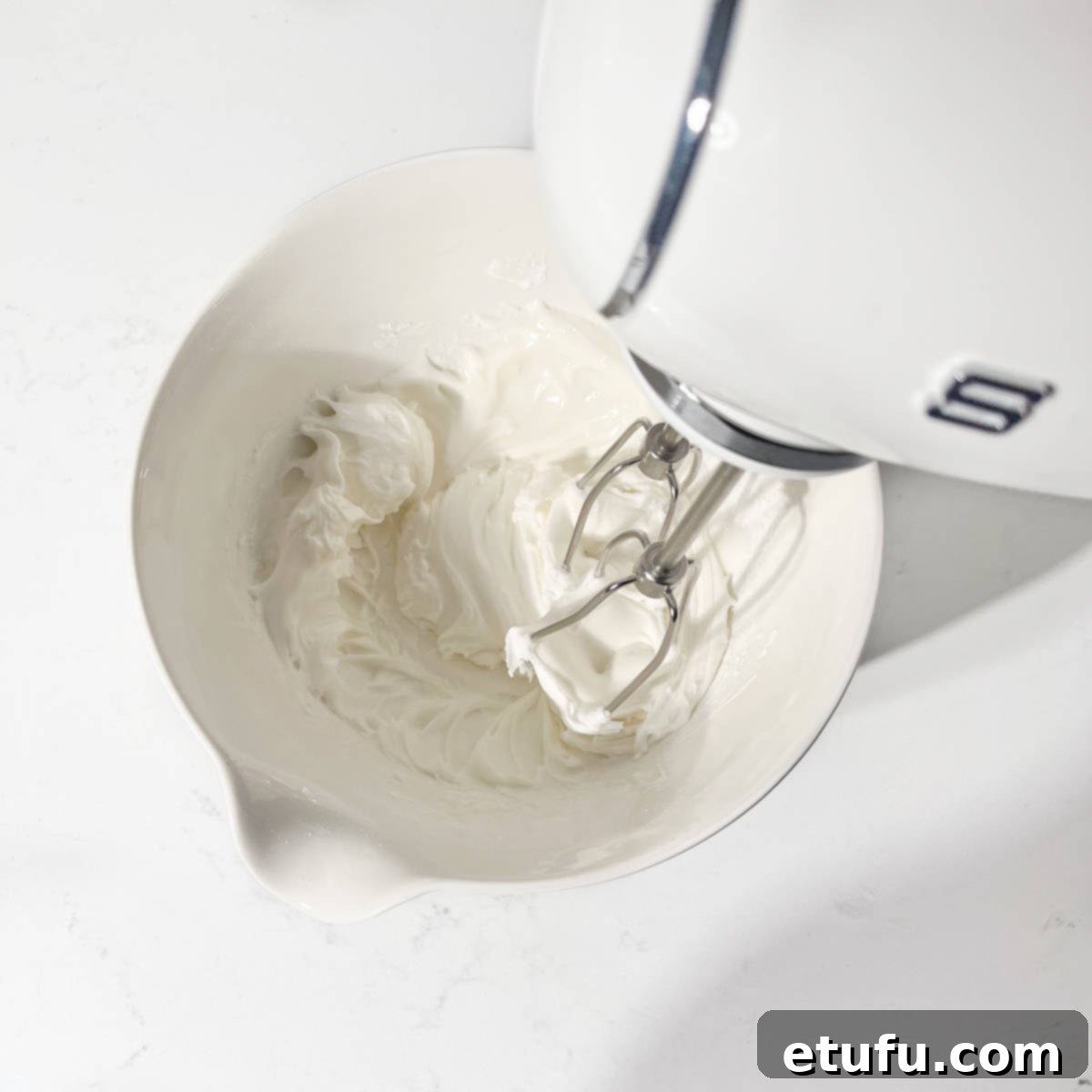 Beating the royal icing with an electric hand mixer for smooth consistency.