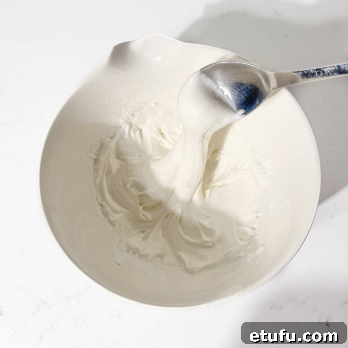 Demonstrating the consistency of piping icing by drizzling icing into a bowl with a spoon, showing it holds its shape.