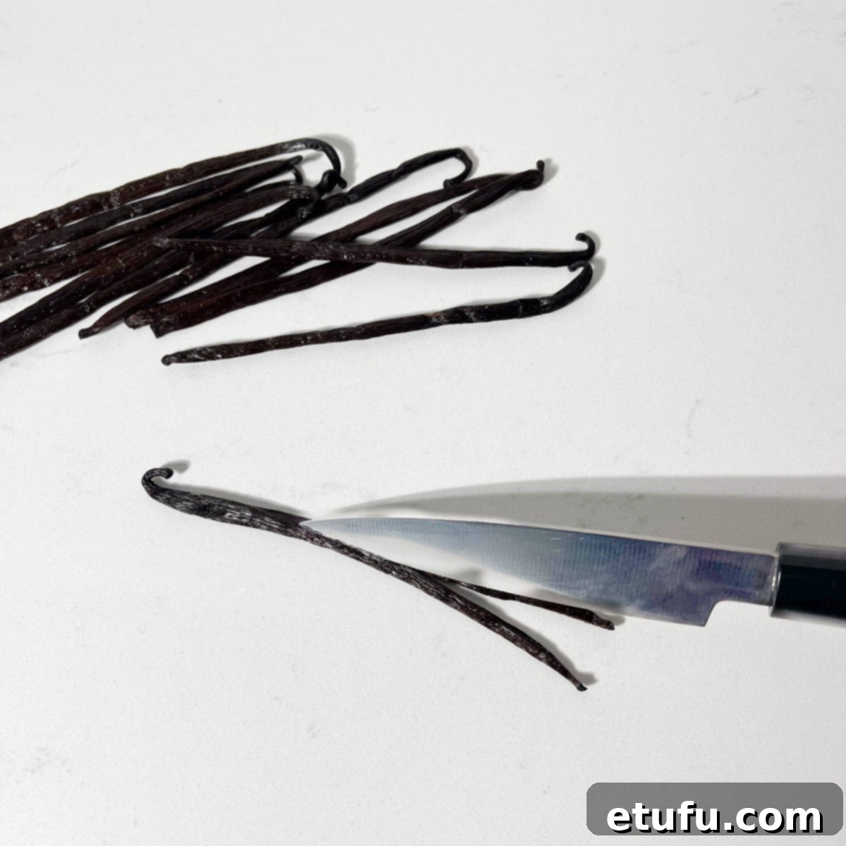 Slicing a vanilla pod in half with a knife.