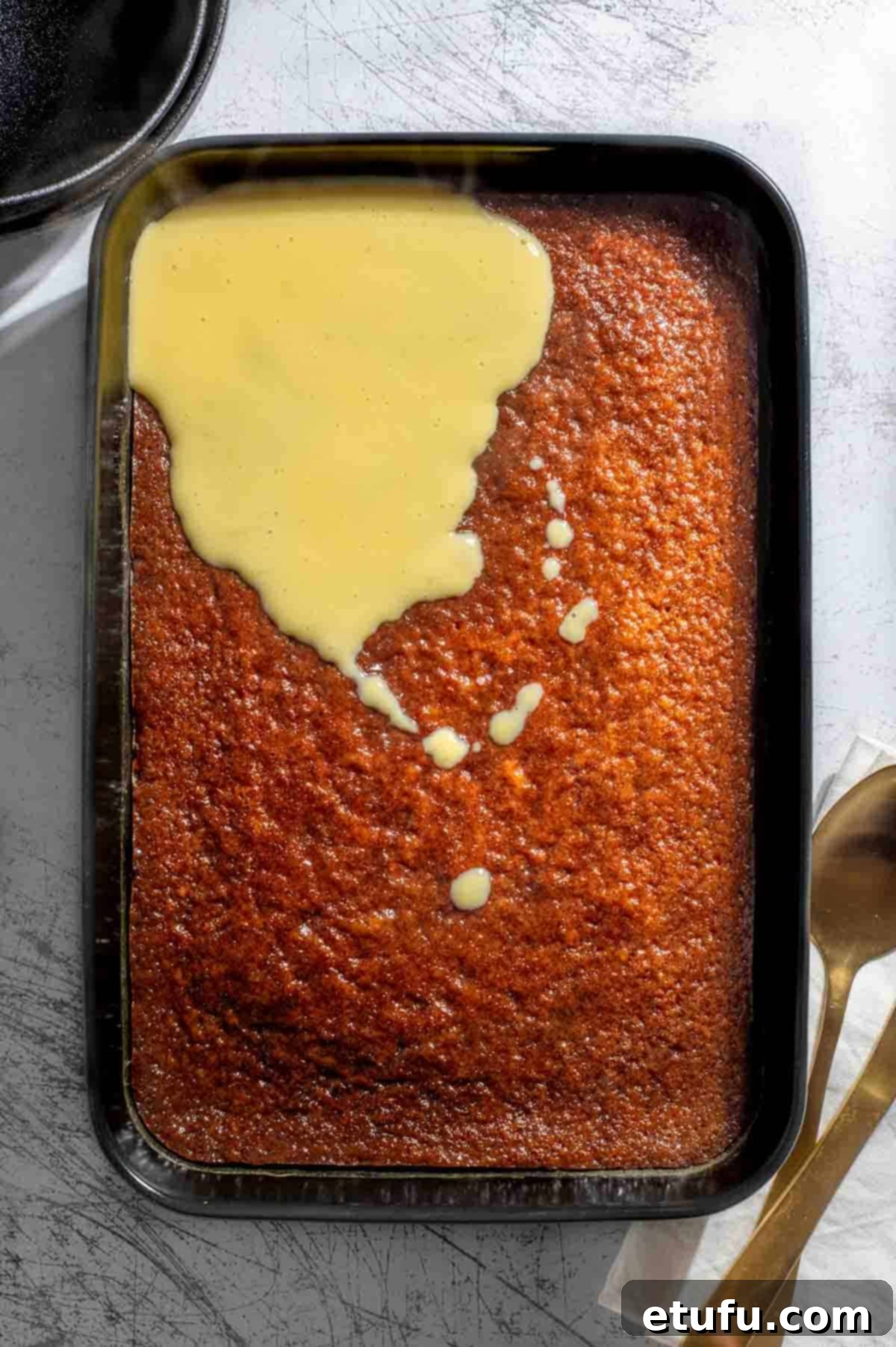 Sticky South African Malva Delight 2 Baked South African Malva pudding in a black baking dish with custard poured over the top.