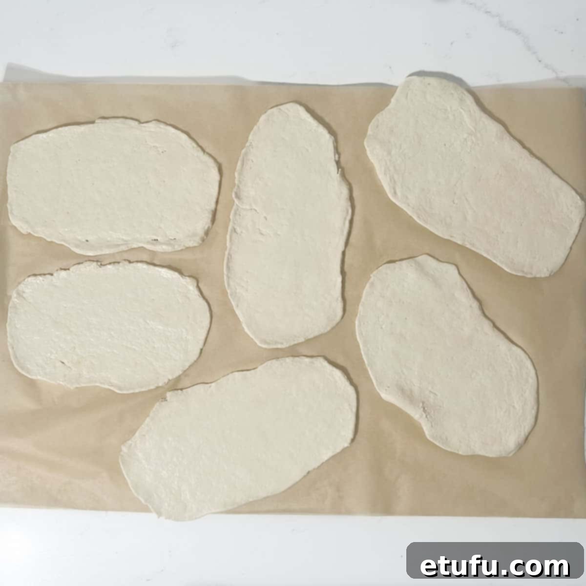 Several rolled-out 2-ingredient flatbreads placed on a sheet of baking paper, ready for cooking.