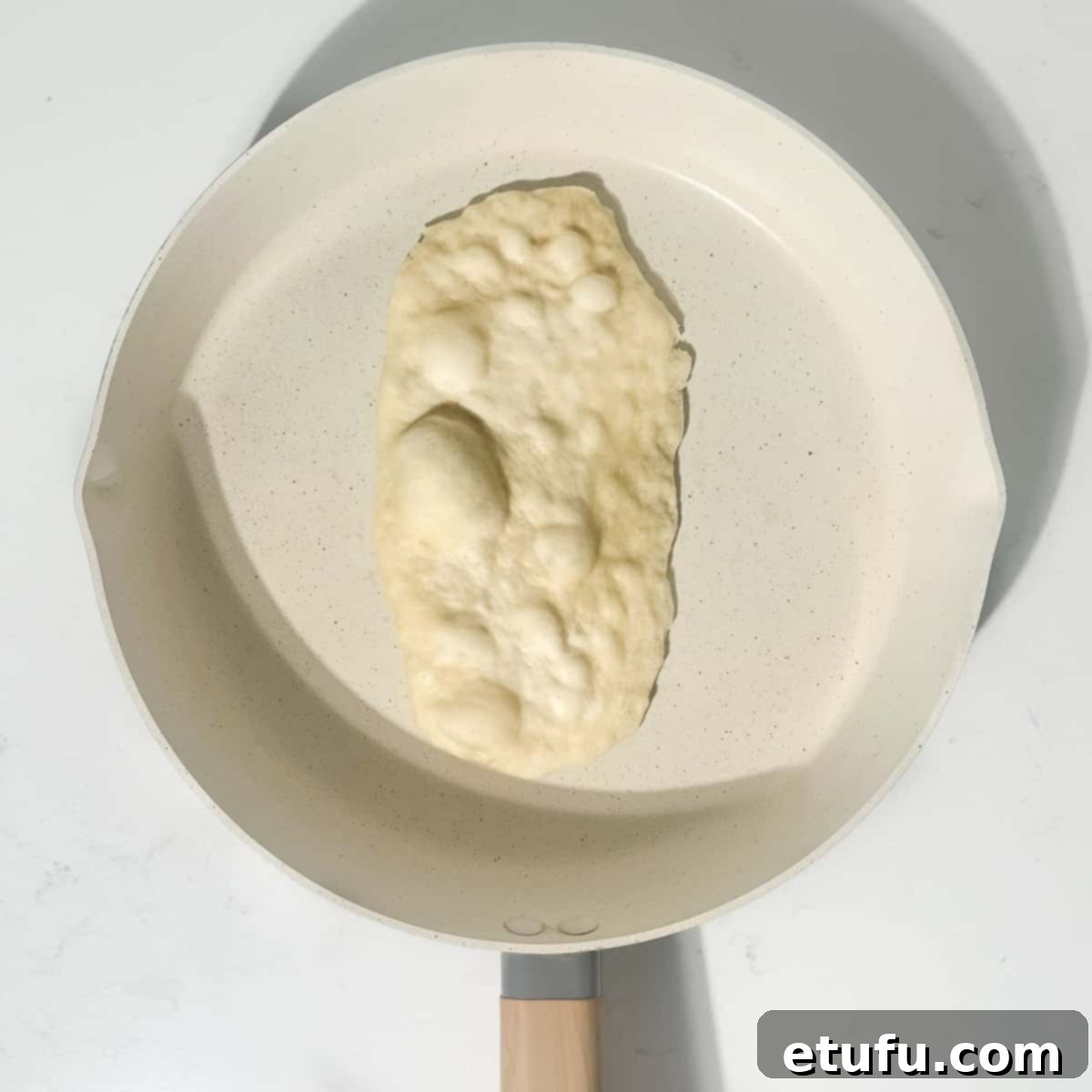 Bubbles forming on the surface of a 2-ingredient flatbread as it cooks in a hot frying pan.