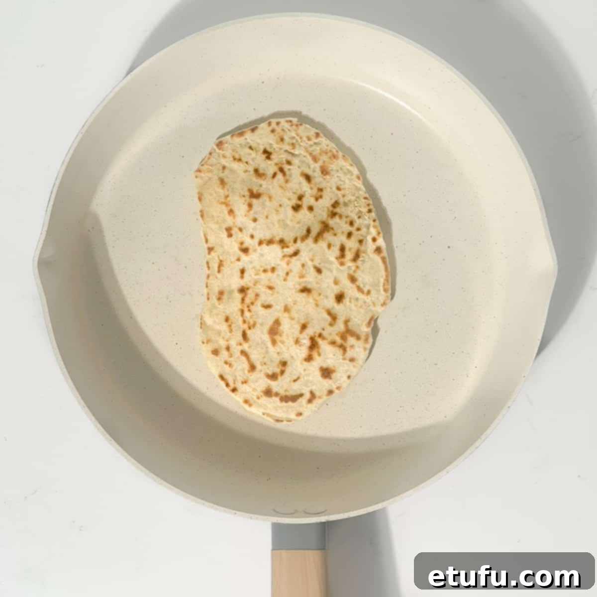 A 2-ingredient flatbread cooking in a large frying pan, showing golden-brown spots.