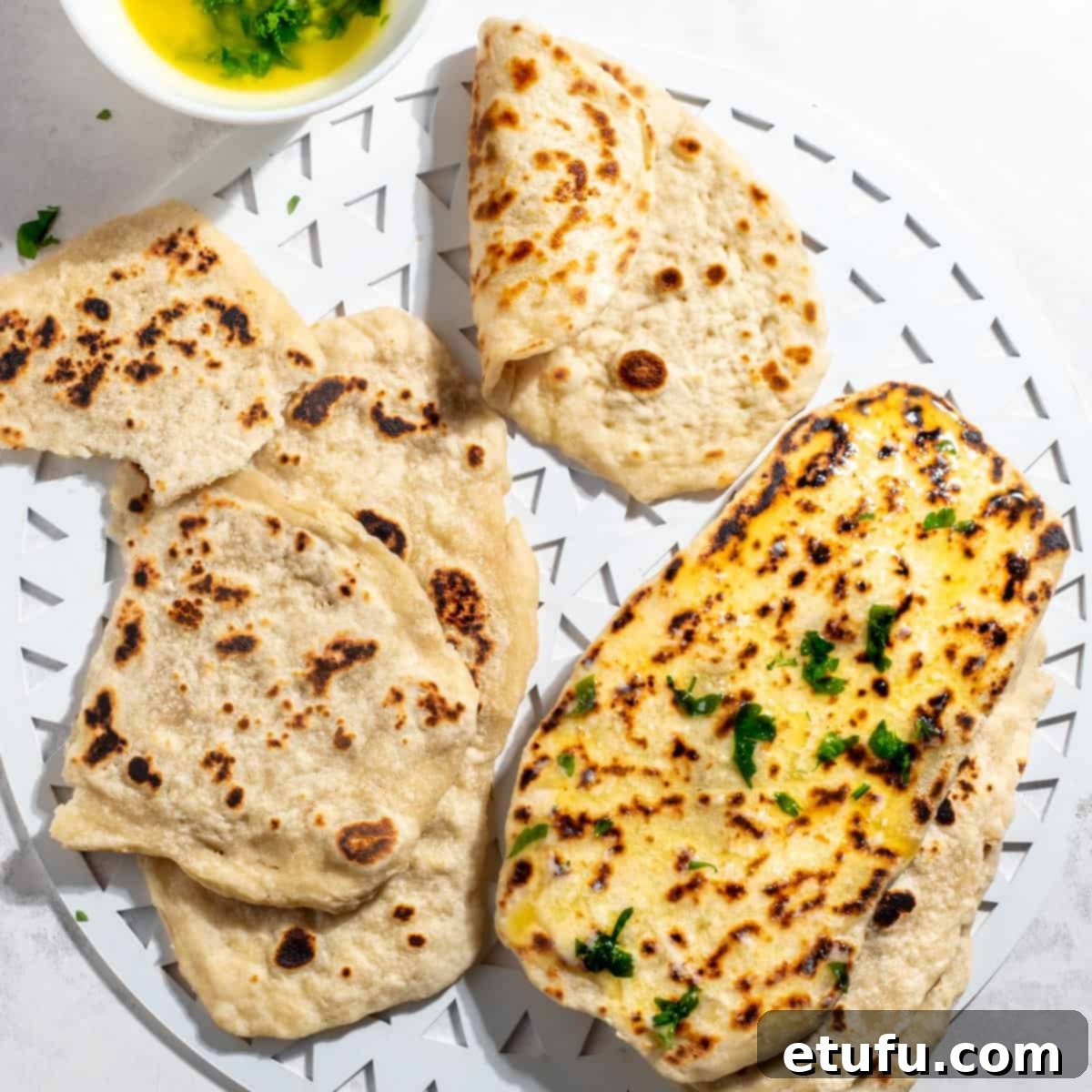 Freshly cooked 2-ingredient flatbreads on a white tray, served with a bowl of vibrant parsley butter on the side.