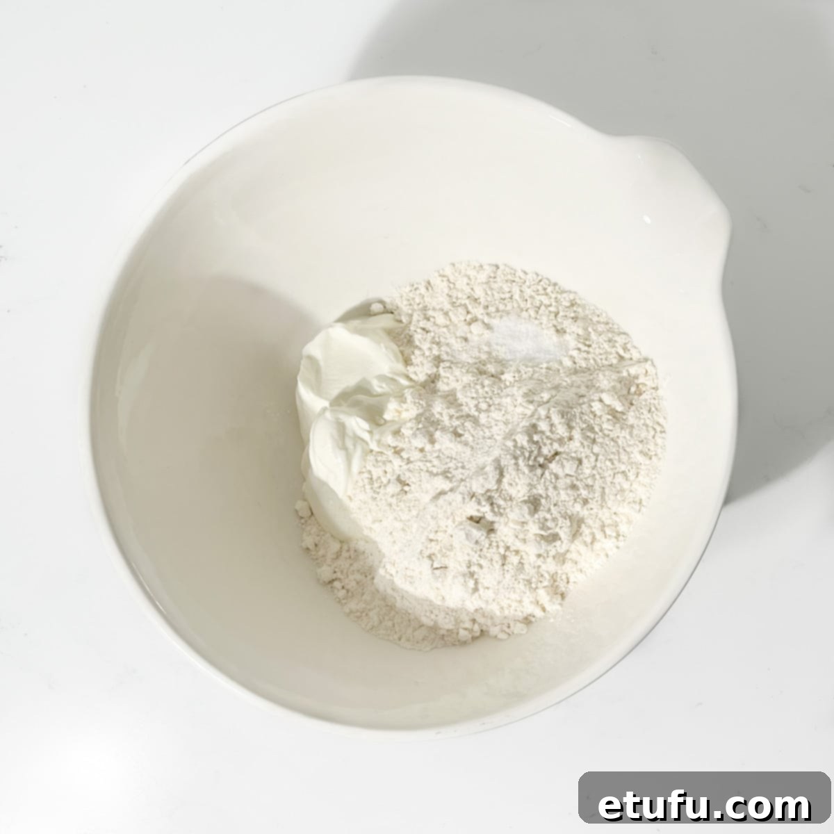 Self-raising flour and Greek yogurt measured and placed in a large white mixing bowl, ready to be combined.