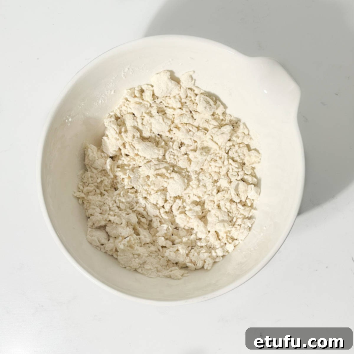 The initial crumbly mixture of flour and yogurt in a bowl, before being fully brought together by hand.