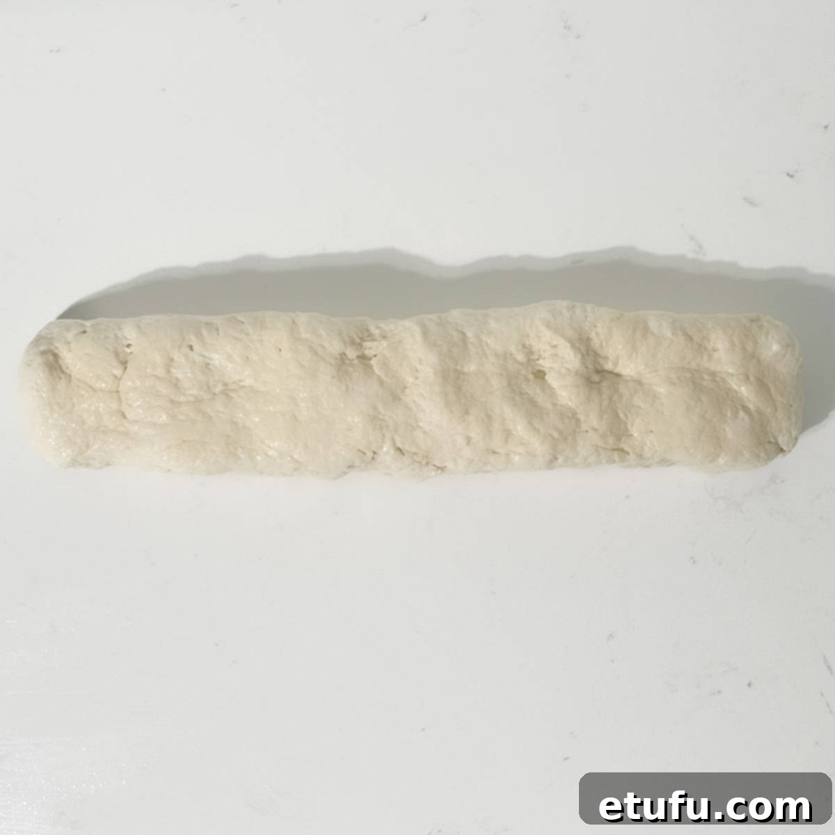 The rested 2-ingredient flatbread dough rolled into a thick sausage shape on a prepared surface.