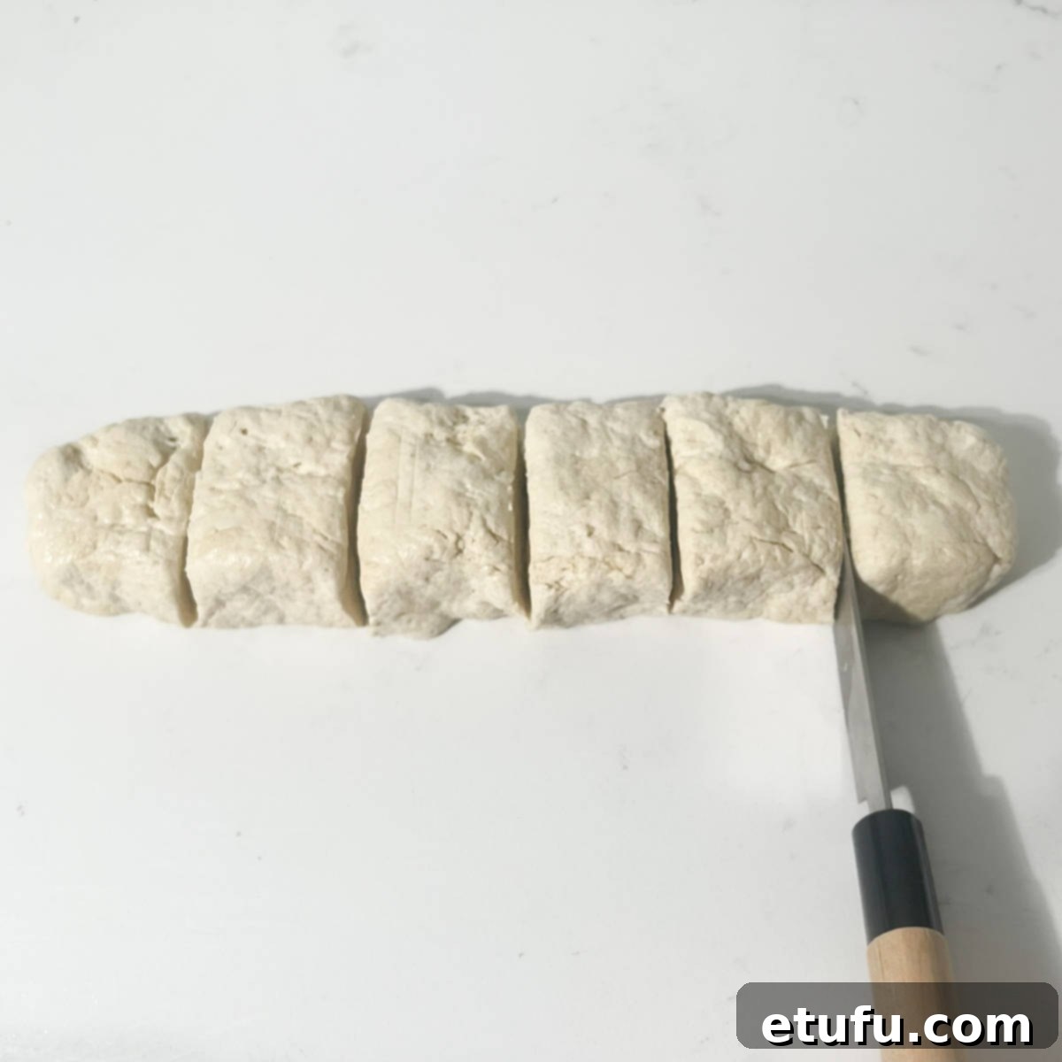 Dividing the sausage-shaped 2-ingredient flatbread dough into six equal pieces with a sharp knife.