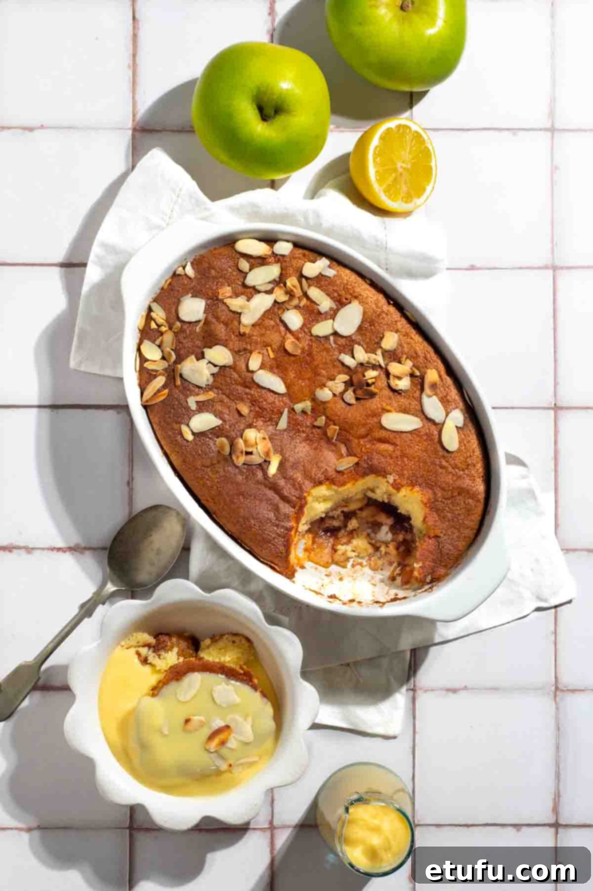 Eve's pudding on a white tiled background with a bowl of eve's pudding topped with custard.