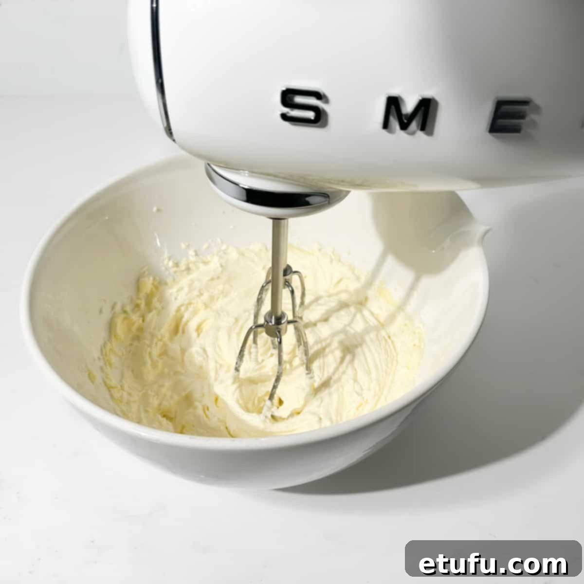 Beating the butter and sugar in a large white bowl with an electric hand mixer.