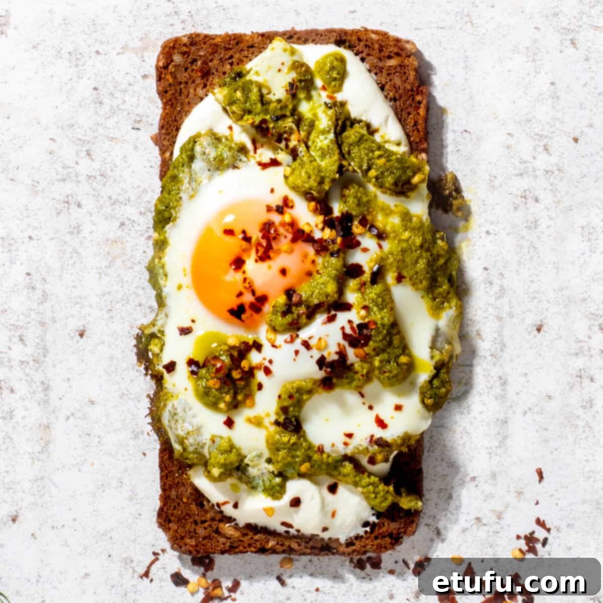 Cottage cheese toast topped with a perfectly fried egg and green pesto, garnished with red chili flakes.
