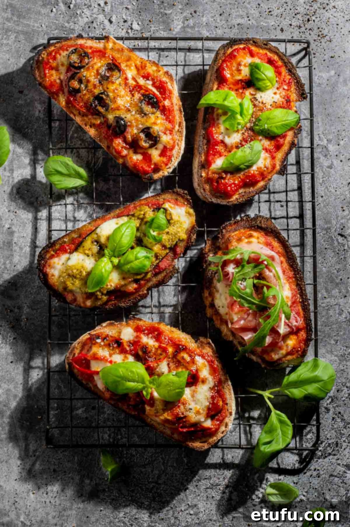 Five types of pizza toast on a cooling rack.