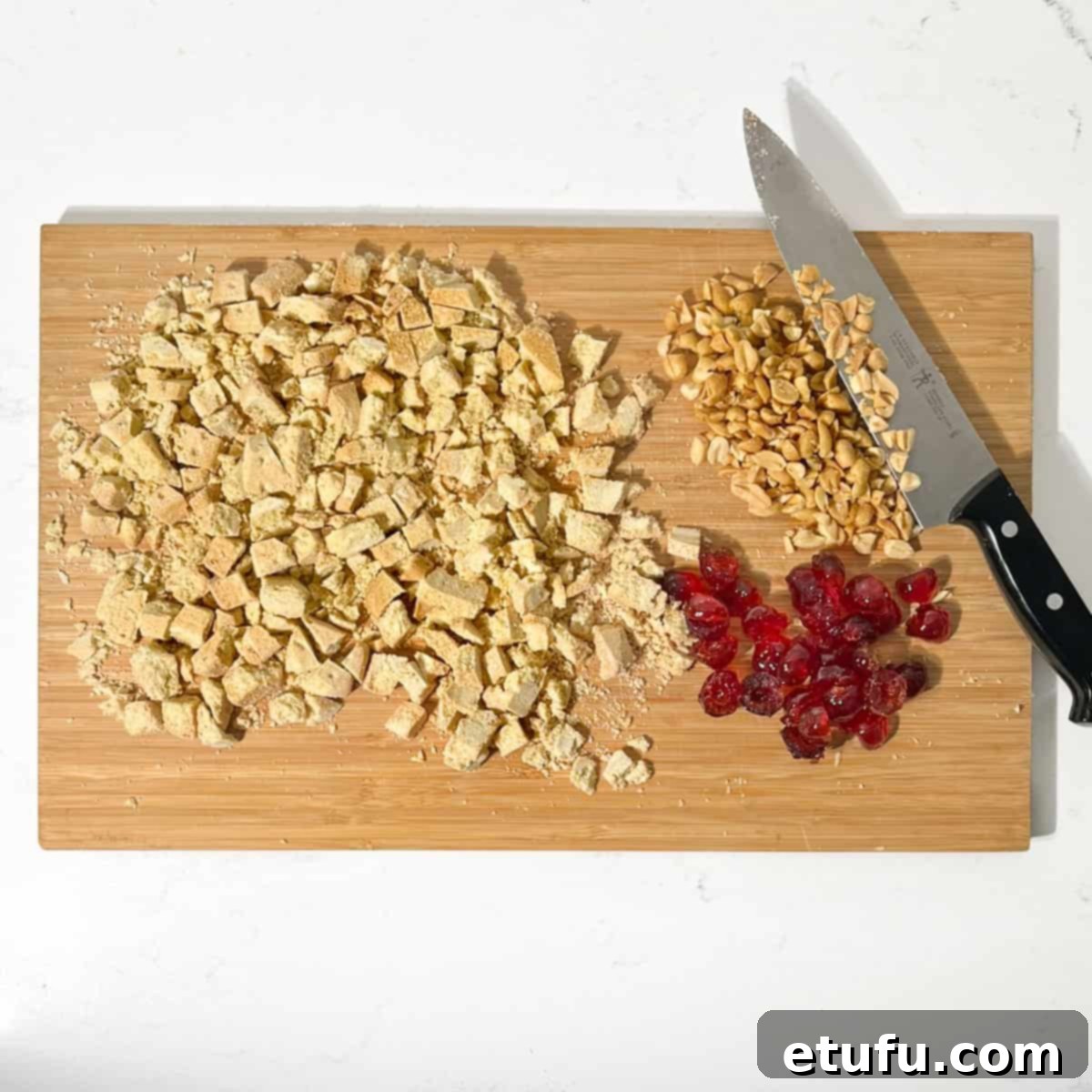 Chopped shortbread, peanuts and glace cherries on a wooden chopping board.