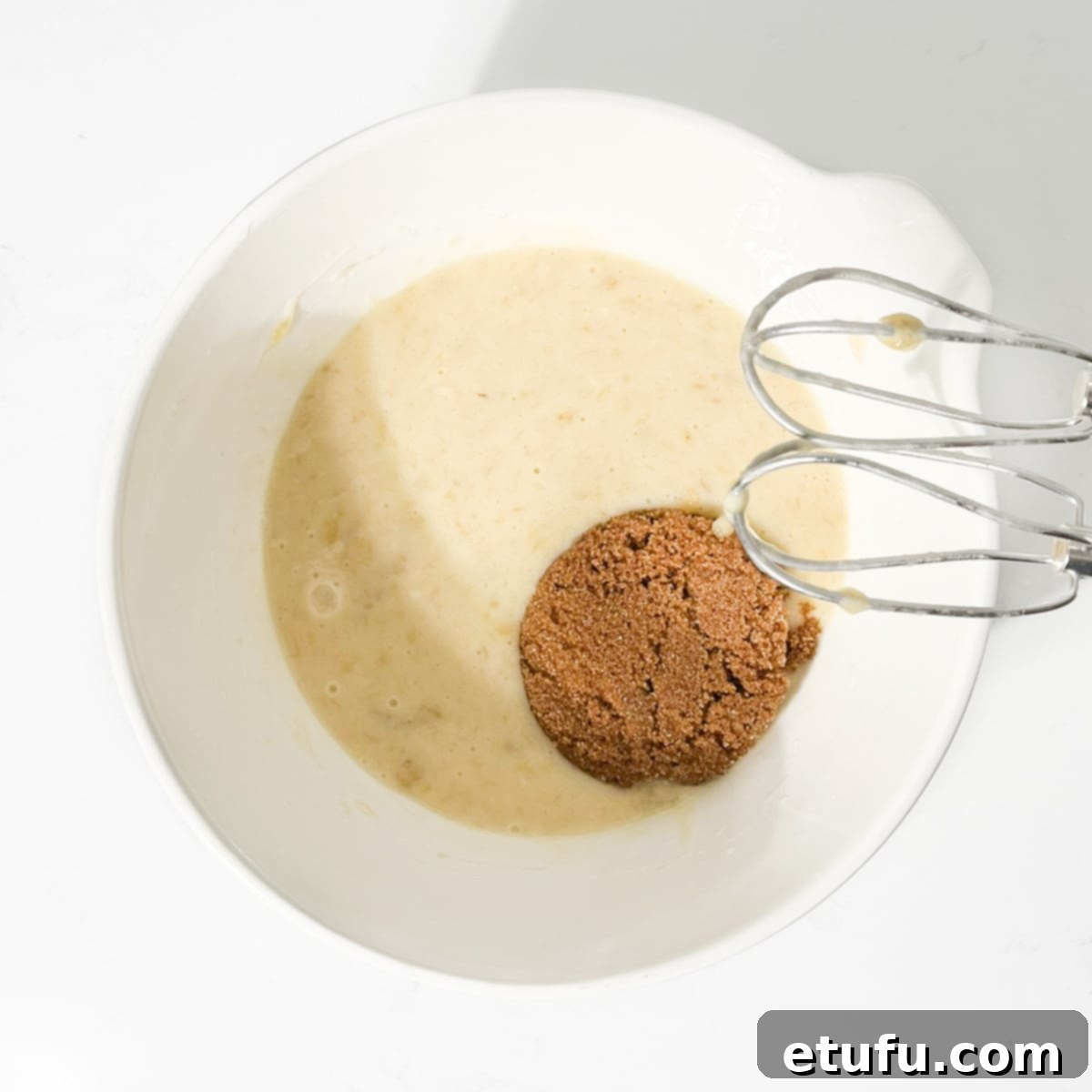 Golden Banana Chocolate Chunk Muffins 12 Adding the brown sugar to the banana and eggs in a large white bowl.