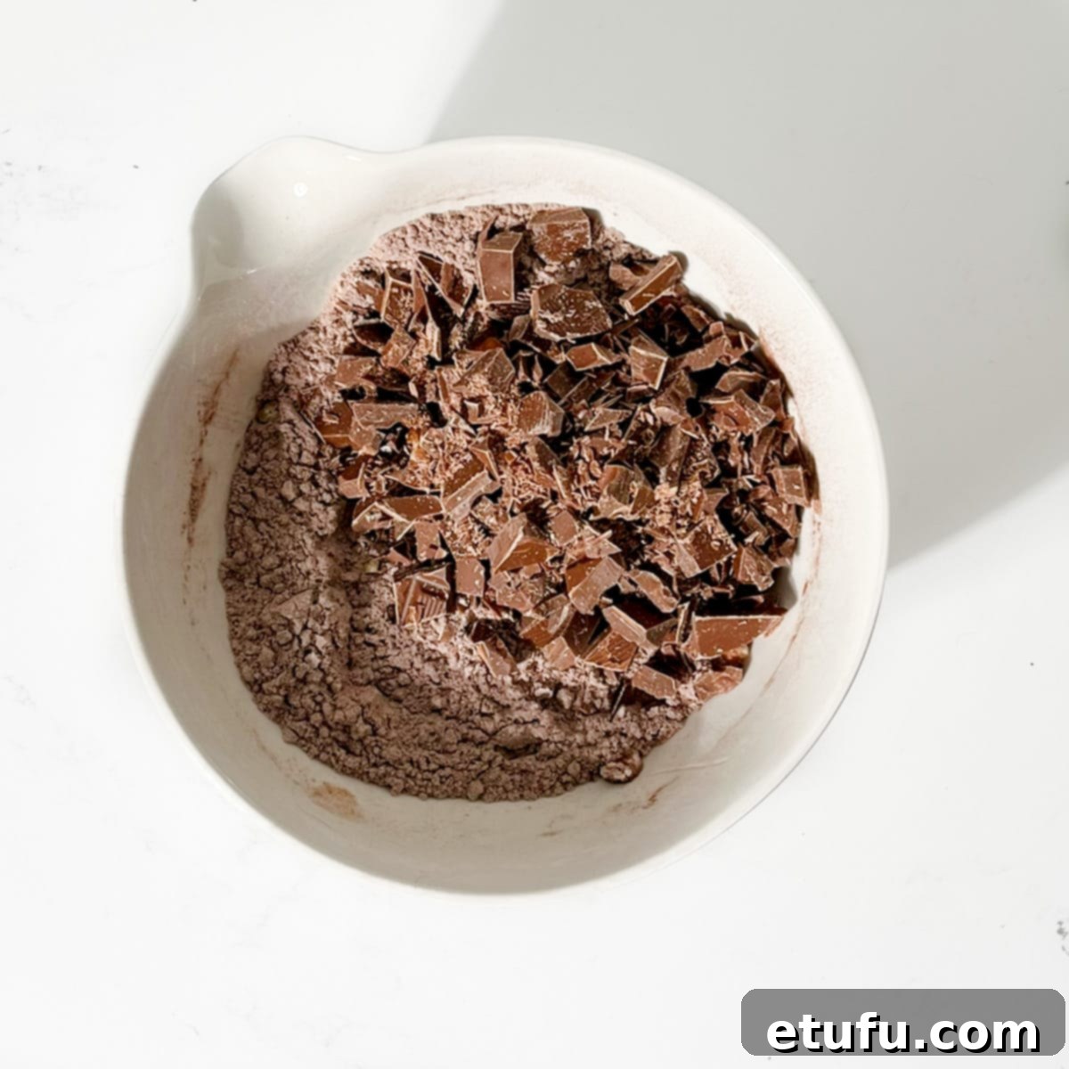 Golden Banana Chocolate Chunk Muffins 15 Adding the chopped chocolate to the flour mixture in a large white bowl.