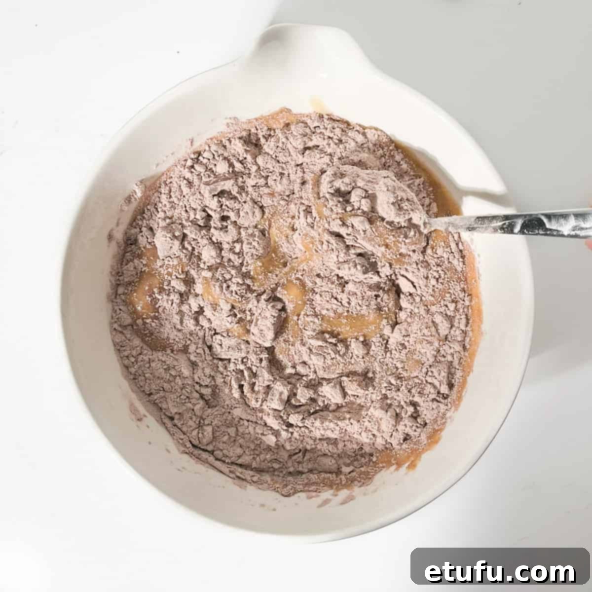 Golden Banana Chocolate Chunk Muffins 17 Folding the dry ingredients into the wet ingredients in a large white bowl.