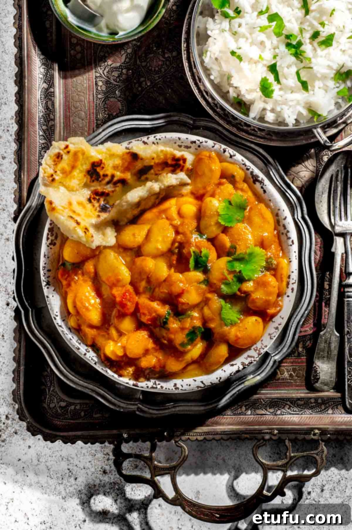 Butter bean curry in a bowl alongside a bowl of rice and a bowl of yoghurt.