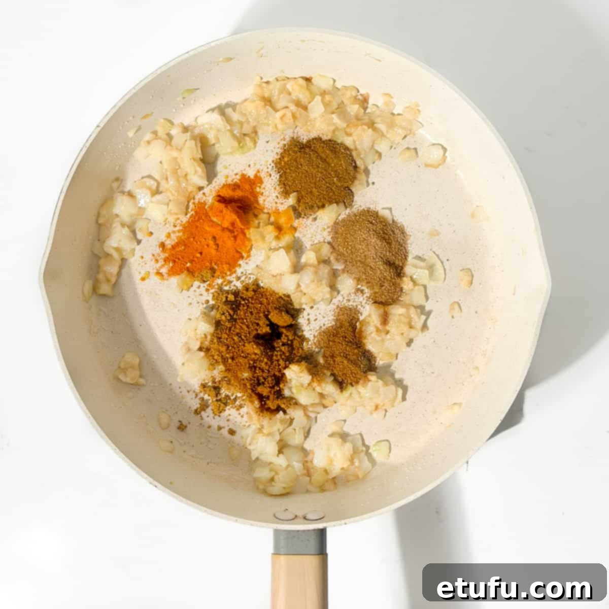 Adding the spices to the onions in a large pan.