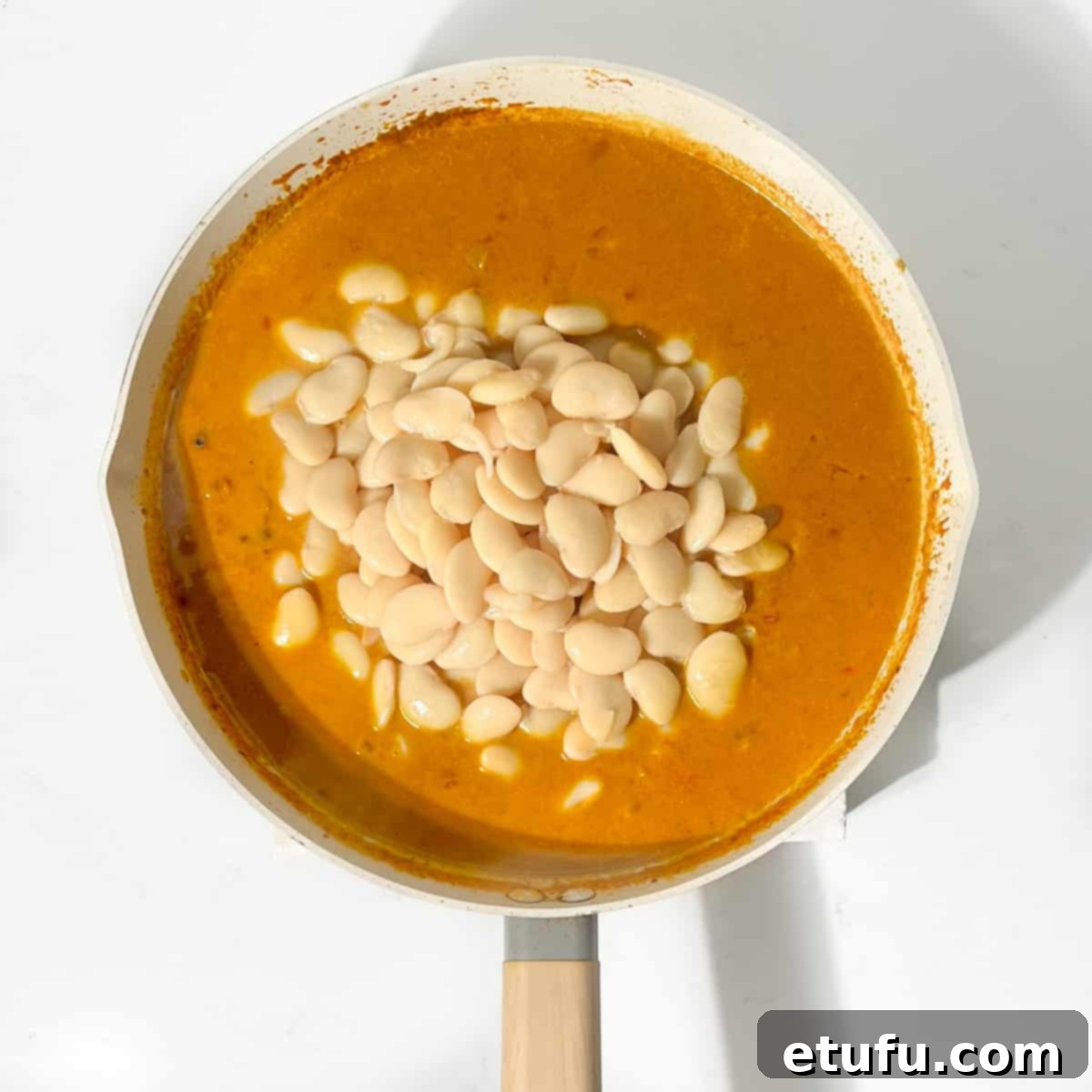 Adding butter beans to the curry sauce in a large pan.