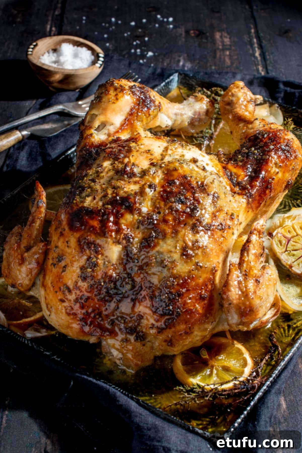 Whole Greek roast chicken on a baking tray, garnished with fresh herbs and lemon slices.