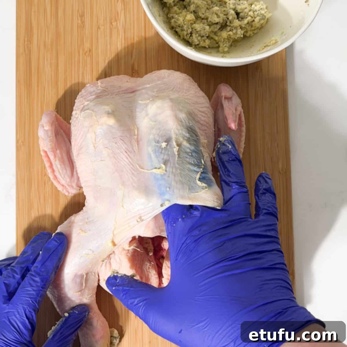 Stuffing dollops of compound butter under the skin of the Greek roast chicken breast.