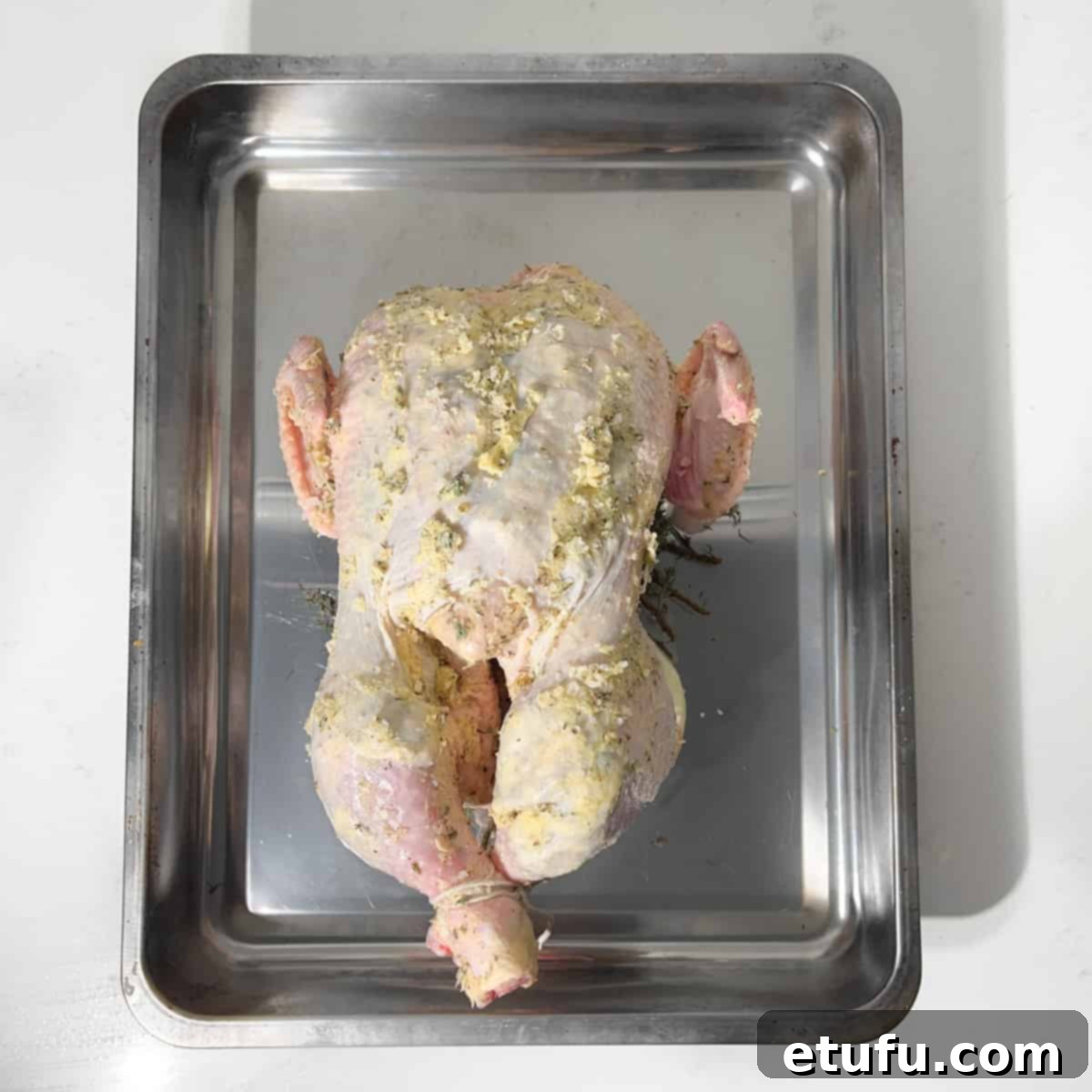 Placing the prepared chicken onto its onion and garlic trivet in the roasting tin.