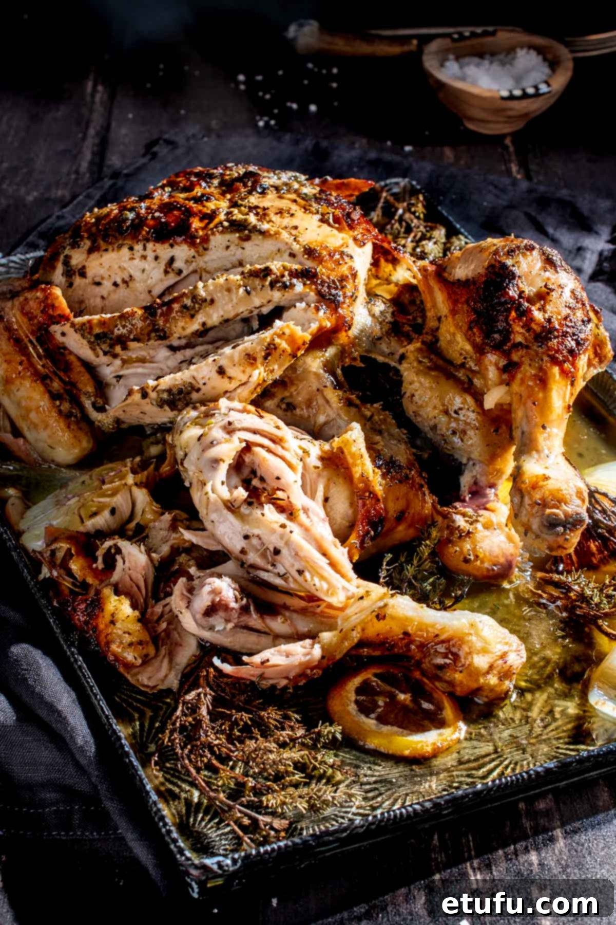 Sliced Greek roast chicken on a baking tray, showcasing its juicy interior and crispy skin.