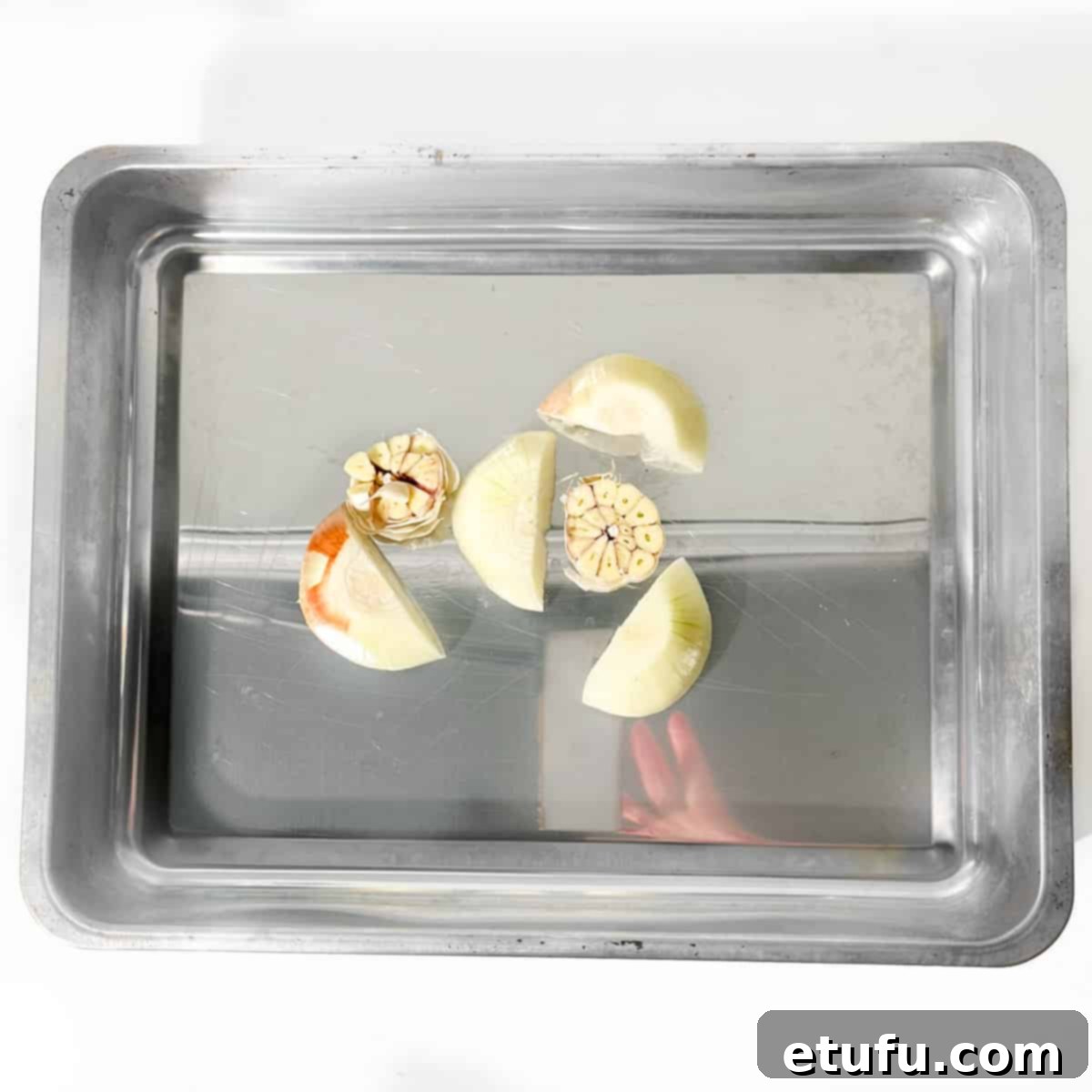 Onion quarters and halved garlic head arranged in a roasting tin, forming a bed.