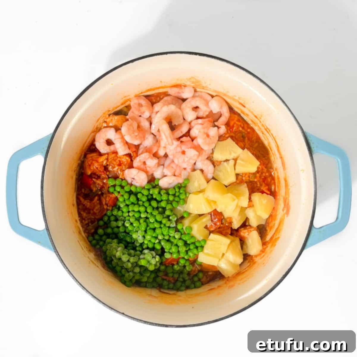 Adding peas, prawns, and pineapple chunks to the jambalaya for the final 5 minutes of cooking, enriching the dish with more color and flavor.