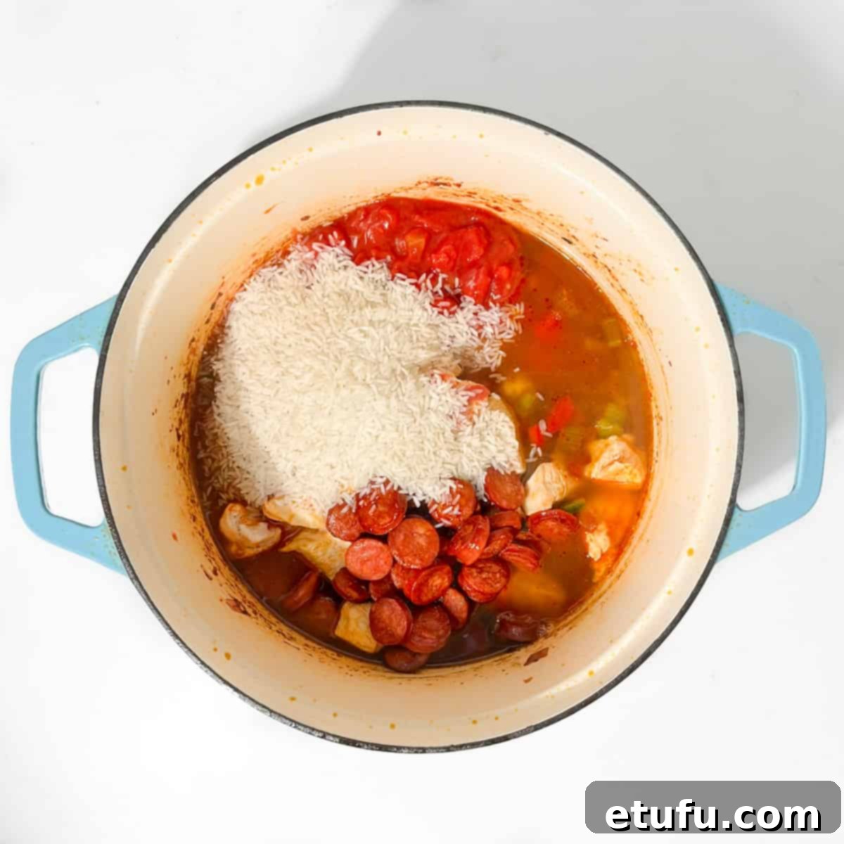 Adding the cooked chorizo, chicken, rinsed rice, and chopped tomatoes to the vegetable and spice mixture in the jambalaya pot.