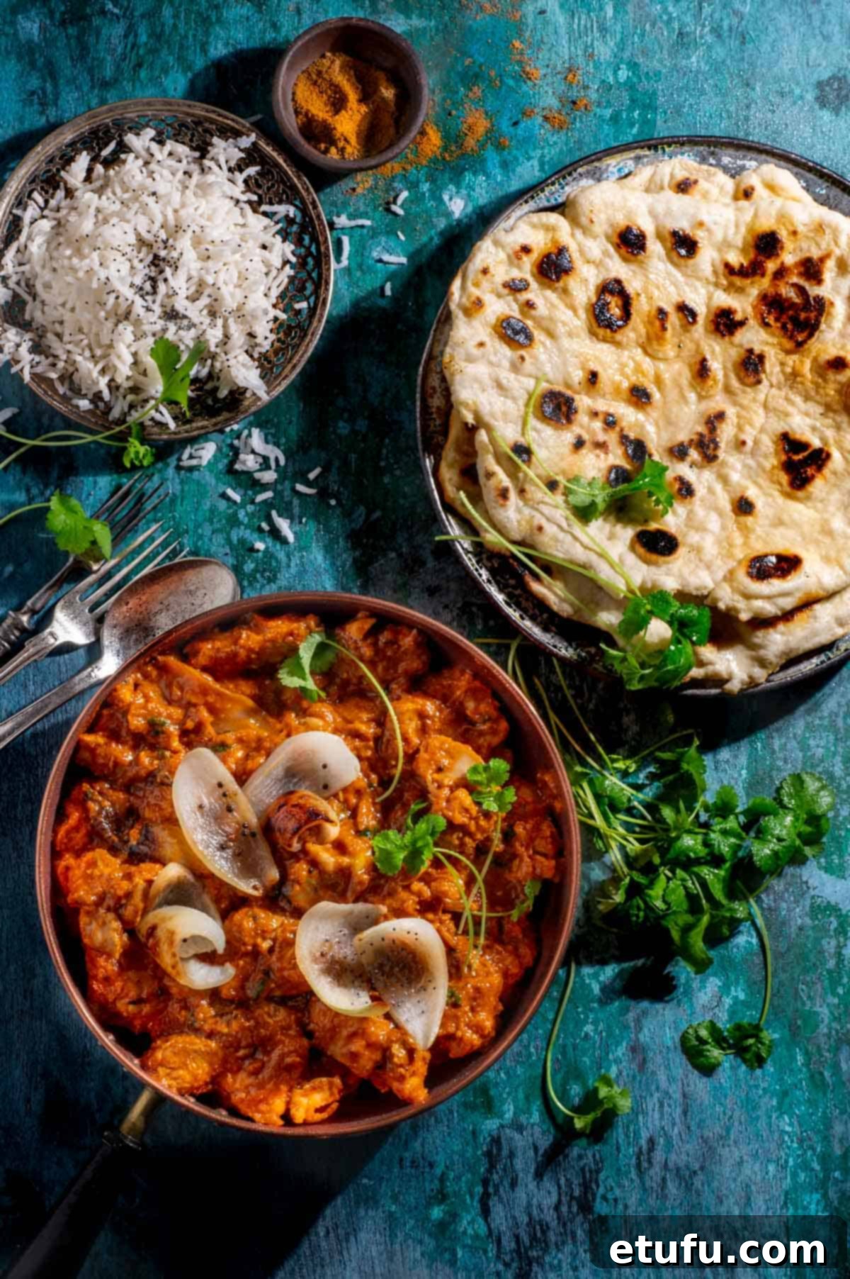 Chicken dopiaza in a copper pan with a plate of flatbreads and a small plate of rice.