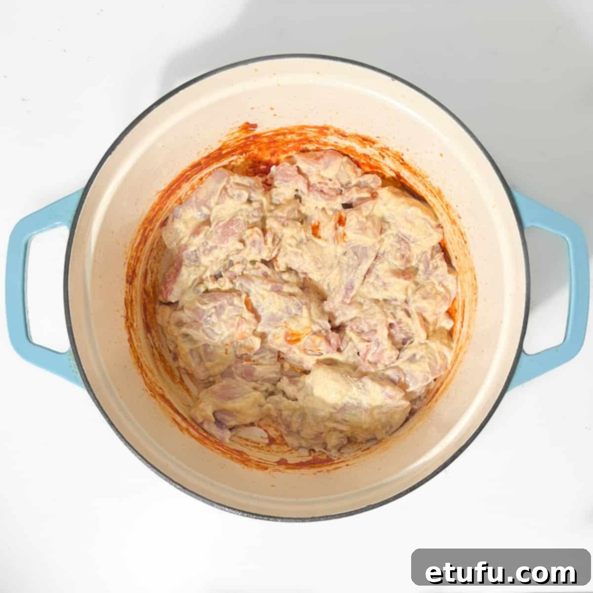 Adding the marinated chicken to the saucepan for browning.