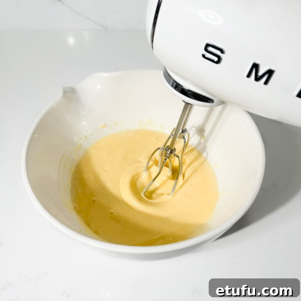 The lemon filling mixture being whisked vigorously with an electric hand mixer until smooth.