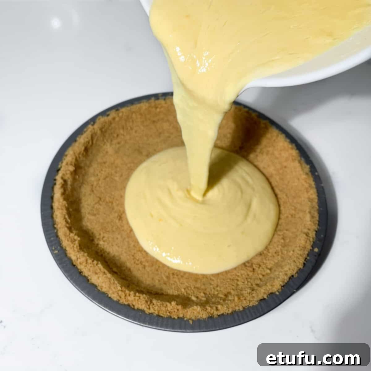 The zesty lemon filling being gently poured into the chilled biscuit base in the tart pan.