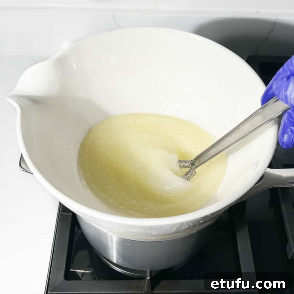 The egg white and sugar mixture being continuously whisked over medium heat in a bain-marie.